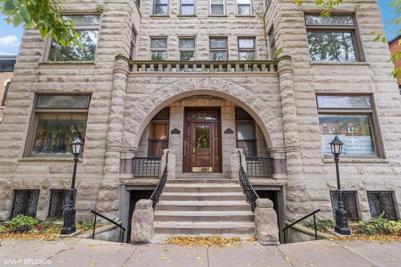 Front view of a multi-story stone building with an arched entrance and stairs leading up to a wooden door.