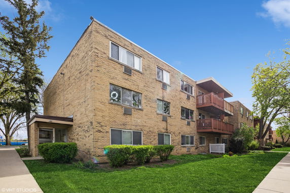 Front view of a three-story brick apartment building with balconies.