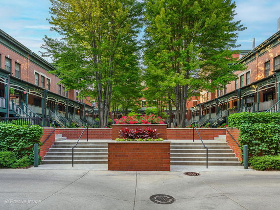 Front view of a row of brick buildings with stairs leading up and trees lining the walkway.