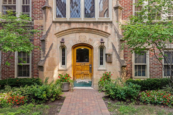 Front view of a brick building entrance with wooden door and decorative stonework.
