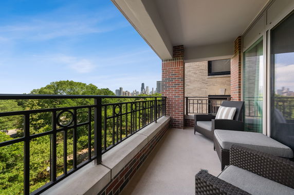 Balcony with seating overlooking cityscape and greenery.