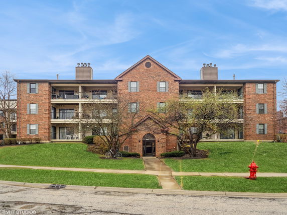 Front view of a three-story brick apartment building with balconies.