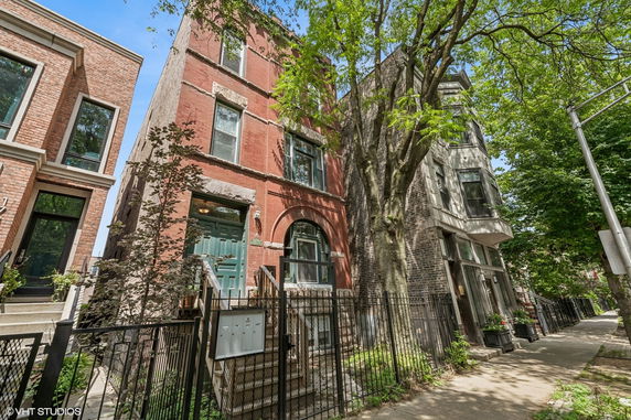 Front view of a three-story brick townhouse with staircase leading to the entrance.