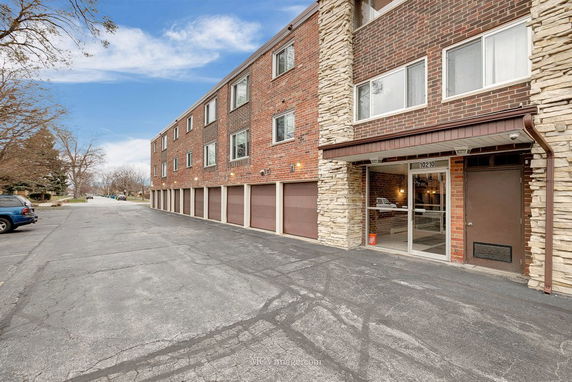 Front view of a multi-story brick building with ground-level garages and a glass entryway.