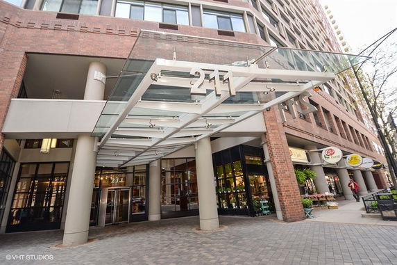 Front view of a multi-story commercial building with a glass canopy and retail shops on the ground floor.