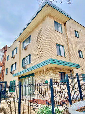 Front view of a multi-story brick building with a wrought iron fence.