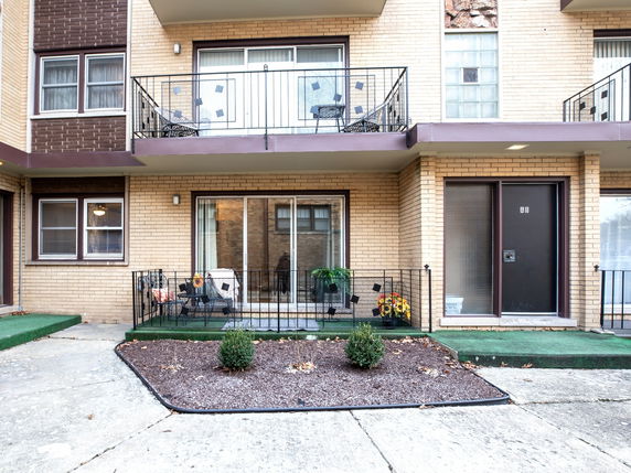 Front view of a multi-story building with balconies and a small garden area.
