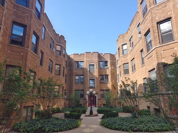 Front view of a brick apartment building with multiple windows and a courtyard.