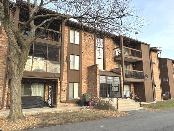 Front view of a multi-story apartment building with balconies and brick exterior.