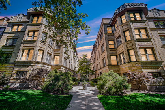 Front view of two adjacent, multi-story brick apartment buildings with large windows.