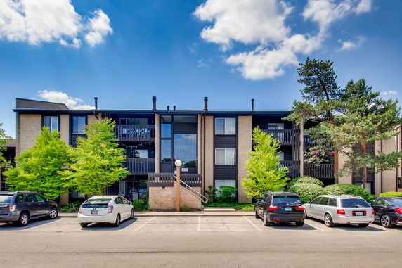 Front view of a three-story residential building with balconies and parking in front.