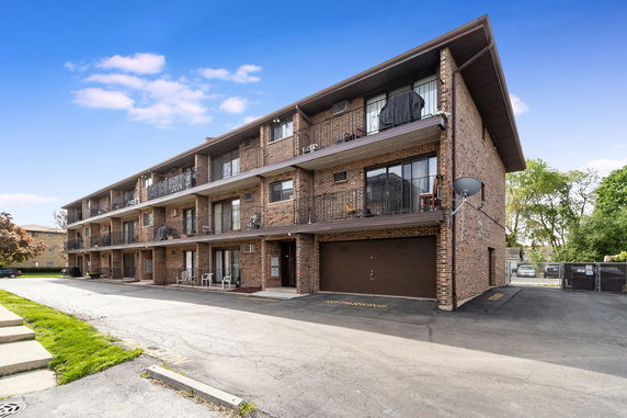 Front view of a three-story brick apartment building with balconies.