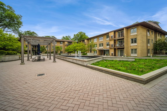 Front view of a multi-story residential building with a paved courtyard and fountain.