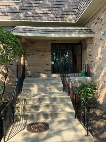 Front view of a brick building with a sloped roof and stairs leading to the entrance.