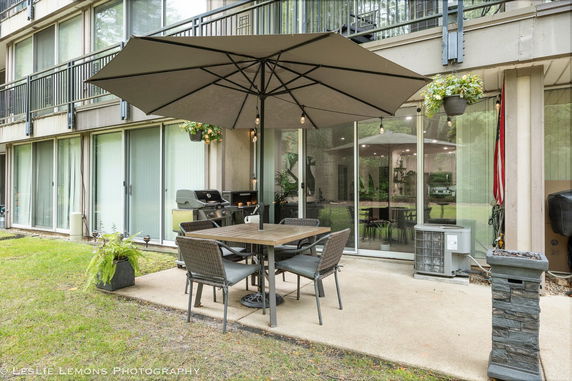 Front view of a building with large glass doors and windows, outdoor seating, and a large umbrella.