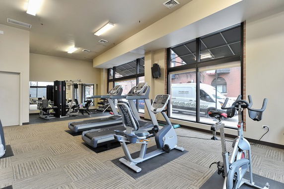 Interior view of a gym with exercise equipment and large windows.