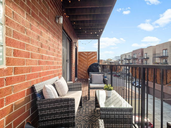 View from a balcony with seating area and string lights, overlooking neighboring buildings.