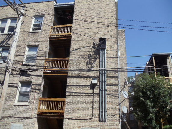 Exterior view of a multi-story brick apartment building with balconies and visible utility lines.