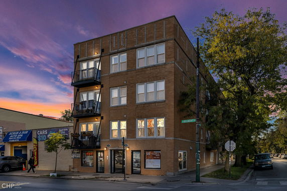 Front view of a multi-story brick building with balconies at sunset.