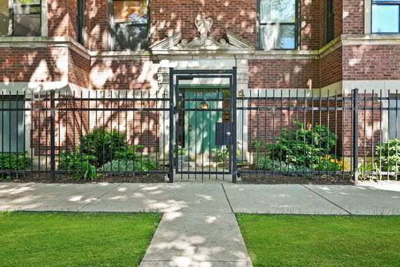 Front view of a brick building with decorative entrance and metal fencing.