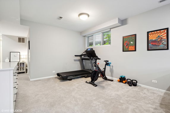 Indoor fitness area with a treadmill and exercise bike against a wall with framed posters.