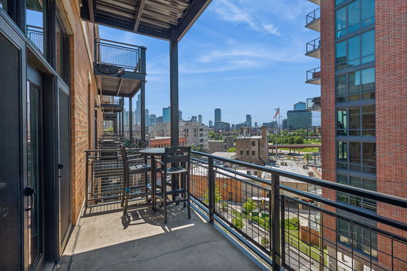 Balcony view with tables and chairs overlooking a cityscape with modern buildings.