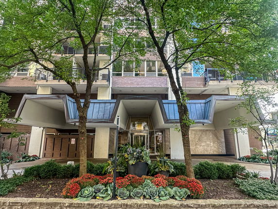 Front view of a multi-story building with balconies and a landscaped entrance.
