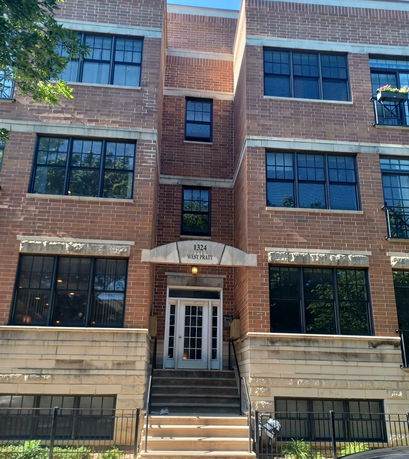 Front view of a multi-story brick building with large windows and a staircase leading to the main entrance.