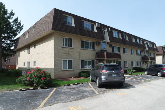 Front view of a three-story apartment building with parking spaces.