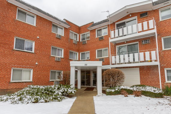 Front view of a multi-story brick apartment building with balconies and a covered entrance.