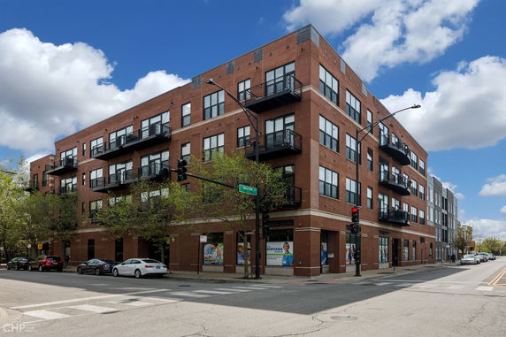 Front view of a multi-story brick building with balconies located on a street corner.