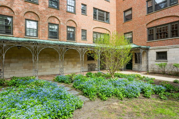 Front view of a brick building with metal archways and a small garden in the foreground.
