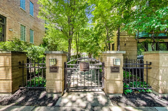 Entrance pathway lined with brick pillars and trees leading to a building.