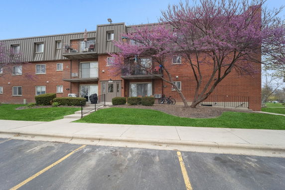 Front view of a three-story brick apartment building with balconies.