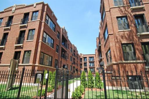 Front view of multiple connected brick apartment buildings with a gated entrance.
