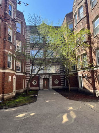 Front view of a multi-story brick building with trees in the courtyard.