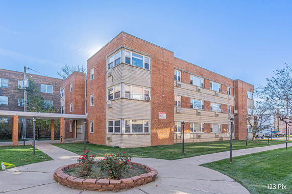 Front view of a three-story brick building with multiple windows and a small garden area.