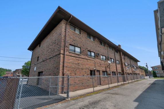 Side view of a multi-story brick apartment building with chain-link fencing.