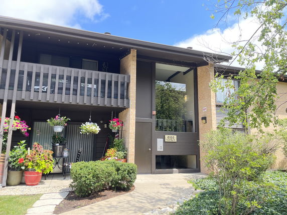 Front view of a multi-story building with balconies and potted plants.