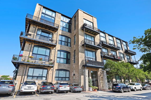 Front view of a multi-story building with balconies and parking area.