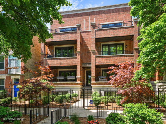 Front view of a multi-story brick building with balconies and a fenced entrance.