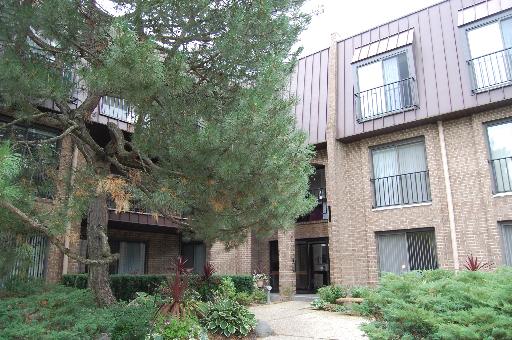 Front view of a multi-story brick building with large windows and a surrounding landscaped area.
