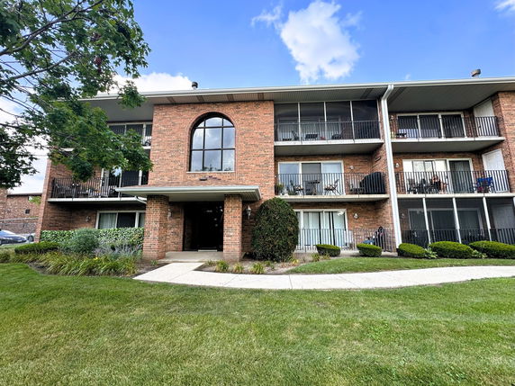 Front view of a three-story brick apartment building with balconies.