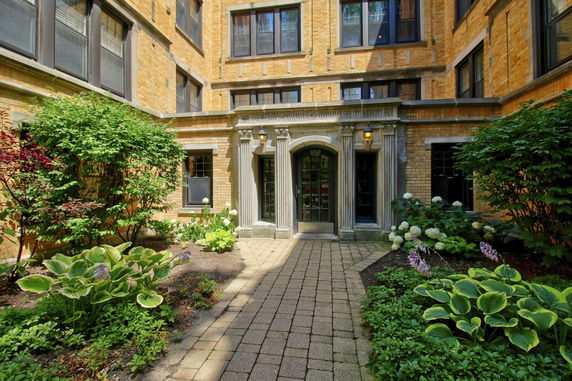 Front view of a brick building with decorative entrance and surrounding plants.