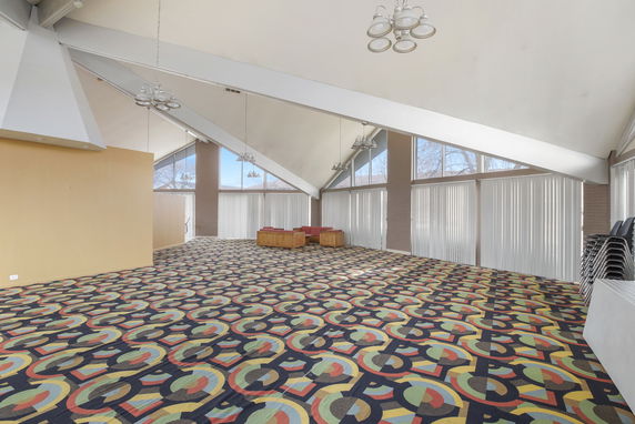Spacious room with patterned carpet and large windows in a clubhouse.