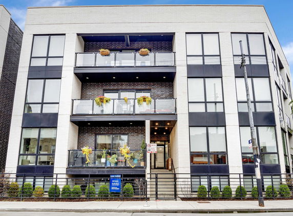 Front view of a modern multi-story building with glass balconies and large windows.