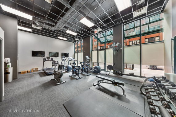 Interior view of a gym with exercise equipment, large windows, and a modern ceiling design.