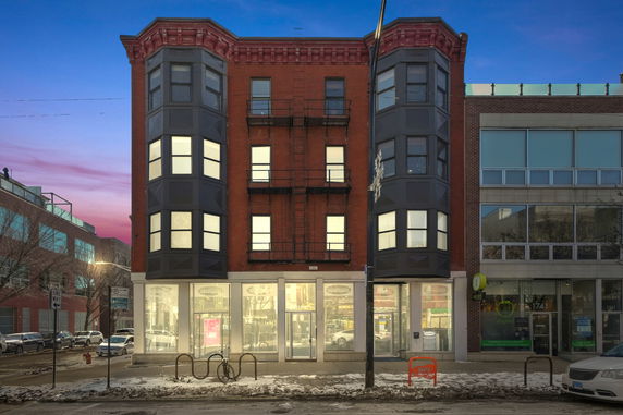 Front view of a multi-story brick building with commercial spaces on the ground floor.