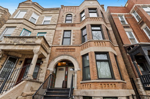 Front view of a multi-story brick townhouse with arched entryway and bay windows.