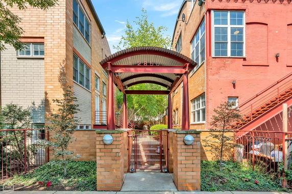 Entrance view of a brick apartment building with a gated pathway and metal archway.